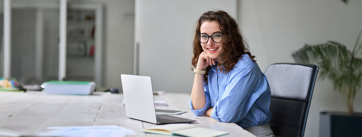 Smiling professional woman at desk with laptop, representing TechForGood as a Certified B Corp and Social Enterprise ICT partner.