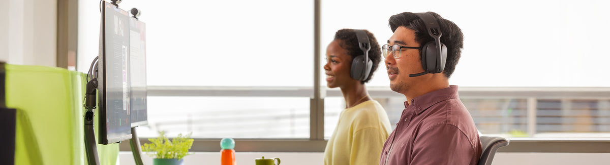 Two professionals wearing headsets at office desks with monitors, focused on work.