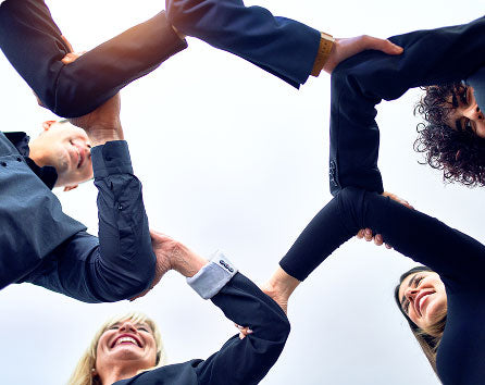 People standing in a circle outdoors with hands joined together overhead