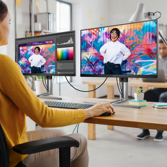 Person working at a desk with two business monitors in an office environment.