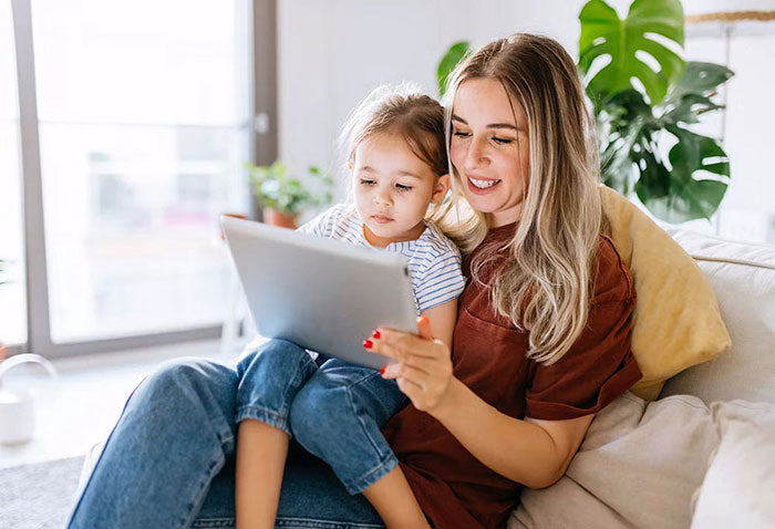 Woman and child sitting on a couch looking at a tablet together.