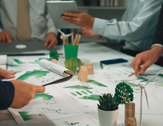 Team reviewing sustainability charts and ESG reports with green graphics, plants, and eco-friendly icons on the table